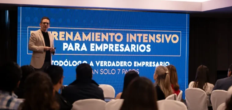 img-Landing-EIPE_24 Un hombre presenta en una conferencia, hablando frente a una audiencia atenta en un ambiente profesional.